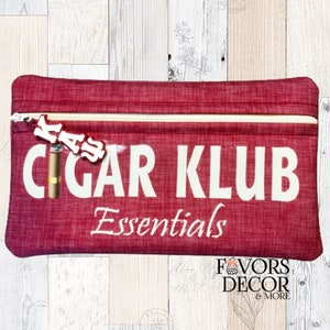 May include: Red zippered pouch with the text "CIGAR KLUB Essentials" in white. The pouch has a small white charm that says "KASS" attached to the zipper.