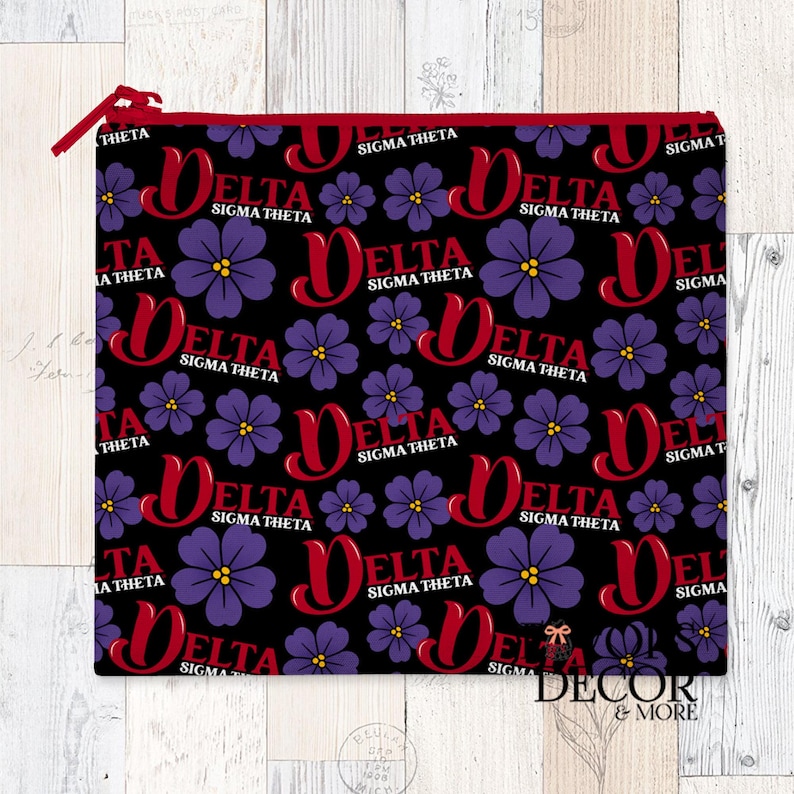 May include: A black zippered pouch with a repeating pattern of purple flowers and the words "DELTA SIGMA THETA" in red. The zipper and trim are red. The pouch is rectangular and likely made of fabric.