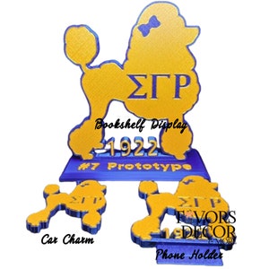 May include: A blue and gold poodle-shaped display with the Greek letters &Sigma;&Gamma;&Rho; and the year 1922. The image includes a bookshelf display, a car charm, and a phone holder, all featuring the same design.