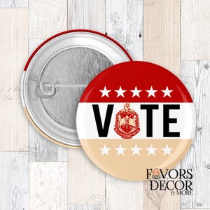 May include: A round button in red, white, and tan, with the word "VOTE" in black. It features a fraternity crest and stars. The button has a pin back and is designed for use as a badge.