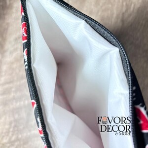May include: Black zippered pouch with a white interior. The exterior features a red and white floral pattern on a black background. The text "FAVORS DECOR & MORE" is printed on the lower right corner.