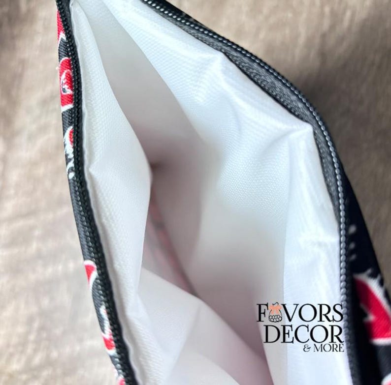 May include: Black zippered pouch with a white interior. The exterior features a red and white floral pattern on a black background. The text "FAVORS DECOR & MORE" is printed on the lower right corner.