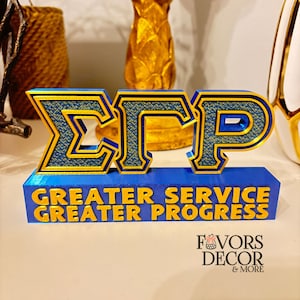 Pu&ograve; includere: Un'insegna decorativa blu e oro con le lettere greche &Sigma;&Gamma;&Rho;. L'insegna include anche le parole "GREATER SERVICE GREATER PROGRESS" in lettere dorate. Si tratta di un oggetto decorativo.