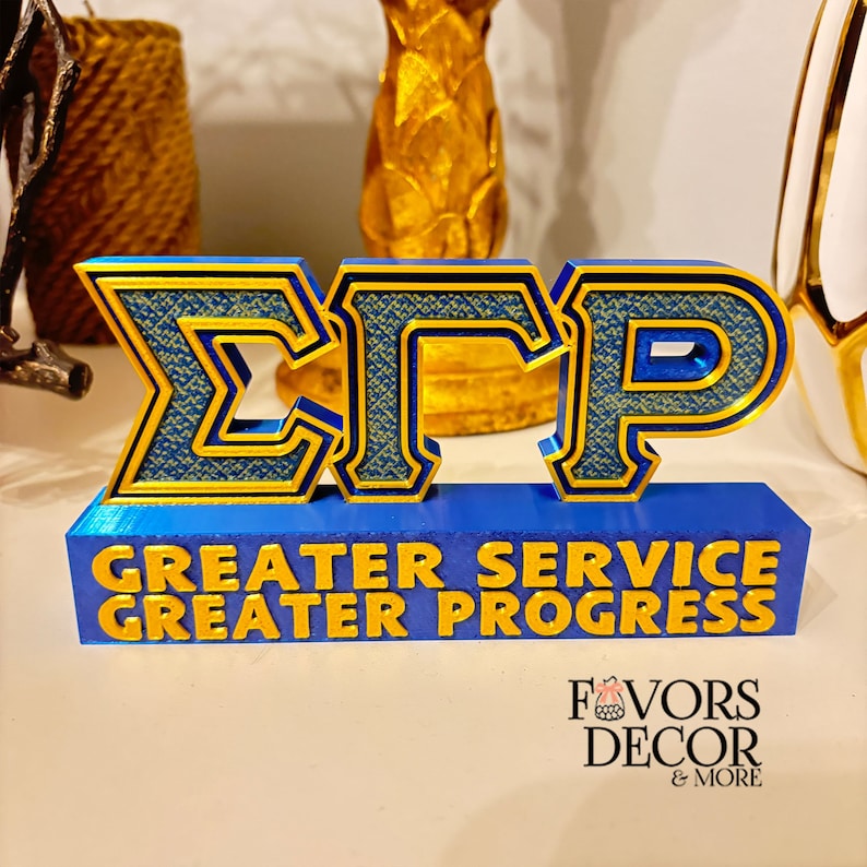 Pu&ograve; includere: Un'insegna decorativa blu e oro con le lettere greche &Sigma;&Gamma;&Rho;. L'insegna include anche le parole "GREATER SERVICE GREATER PROGRESS" in lettere dorate. Si tratta di un oggetto decorativo.