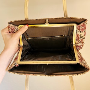 Peut inclure: Sac &agrave; main vintage en tapisserie avec un motif floral rouge, beige et marron. Il est dot&eacute; d'un cadre dor&eacute; et de poign&eacute;es cr&egrave;me. L'int&eacute;rieur est doubl&eacute; de tissu marron fonc&eacute; et le cadre est dot&eacute; d'une fermeture &agrave; fermoir. Le design du sac &eacute;voque une &eacute;poque r&eacute;volue.