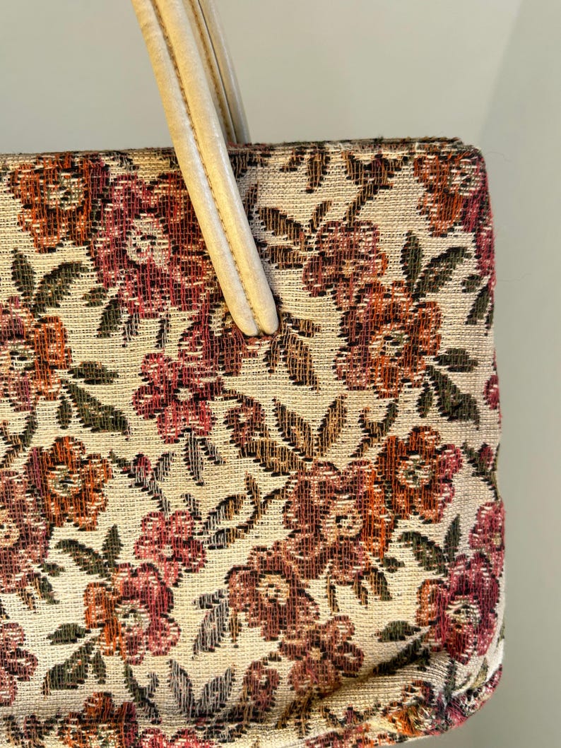 Peut inclure: Sac &agrave; main vintage avec un motif floral en tapisserie dans les tons de rouge, orange et vert sur fond cr&egrave;me. Le sac est de forme rectangulaire avec une poign&eacute;e cr&egrave;me.