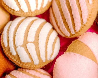 Può includere: Primo piano di diversi pasticcini concha, un tradizionale pane dolce messicano. I pasticcini hanno una forma rotonda con una copertura strutturata e a strisce in bianco o rosa, su uno sfondo rosa vibrante. La base del pane è di colore marrone chiaro.