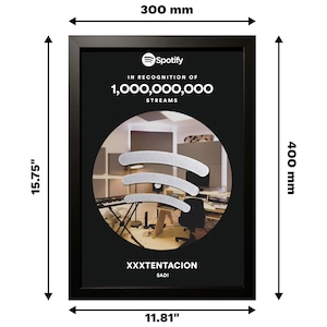 May include: Black framed plaque with a silver Spotify logo and the text "IN RECOGNITION OF 1,000,000,000 STREAMS" and "XXXTENTACION SAD!"  The plaque has a photo of a recording studio inside the Spotify logo.
