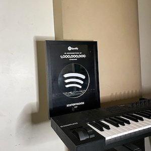 May include: A black framed plaque with a white Spotify logo and the text "In recognition of 1,000,000,000 streams" and "XXXTENTACION".