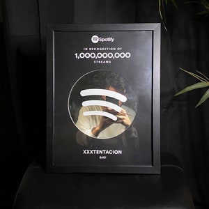 May include: Black framed plaque with a white Spotify logo and the text "In recognition of 1,000,000,000 streams". A circular mirror with the Spotify logo reflected in it is in the center. The text "XXXTENTACION" and "SAD!" is at the bottom.