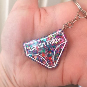 May include: A colourful glitter keychain shaped like underwear with the text "Big Girl Pants" in white lettering.