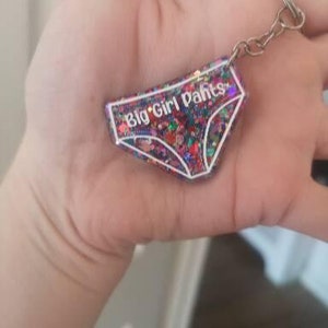 May include: A colourful glitter keychain shaped like underwear with the text "Big Girl Pants" in white.