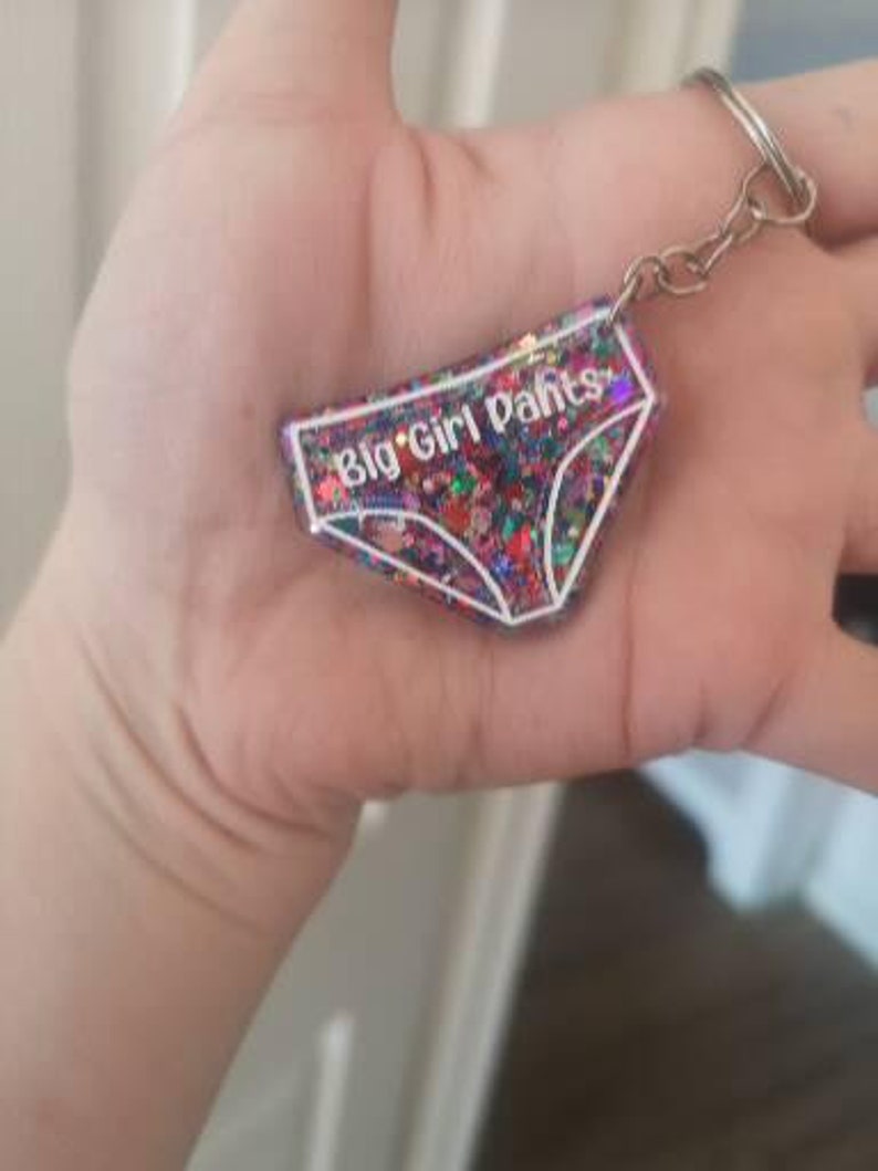 May include: A colourful glitter keychain shaped like underwear with the text "Big Girl Pants" in white.