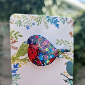 Peut inclure: Une broche en forme de rouge-gorge en paillettes rouges, bleues et vertes. Le rouge-gorge est un symbole populaire de No&euml;l et d'hiver.