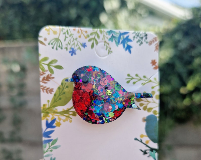 Peut inclure: Une broche en forme de rouge-gorge en paillettes rouges, bleues et vertes. Le rouge-gorge est un symbole populaire de No&euml;l et d'hiver.