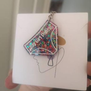 May include: A colourful glitter keychain shaped like a pair of underwear with the text "Big Girl Pants" on it.