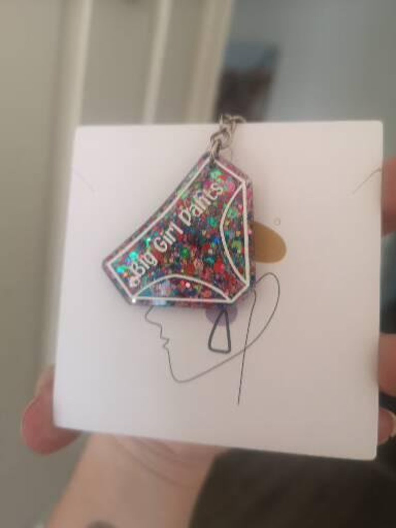May include: A colourful glitter keychain shaped like a pair of underwear with the text "Big Girl Pants" on it.