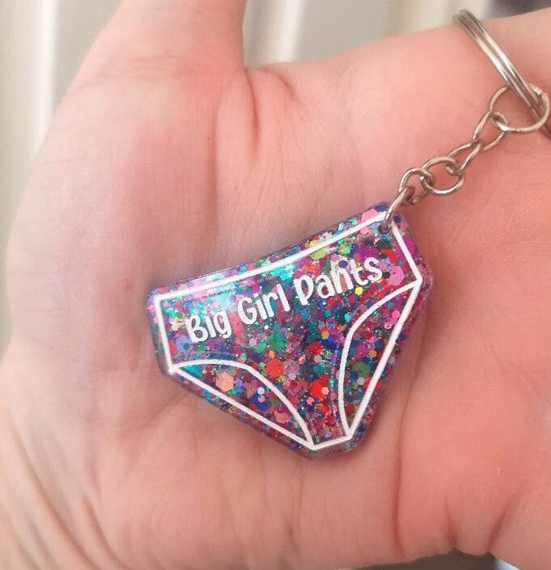 May include: A colourful glitter keychain shaped like underwear with the text "Big Girl Pants" in white lettering.