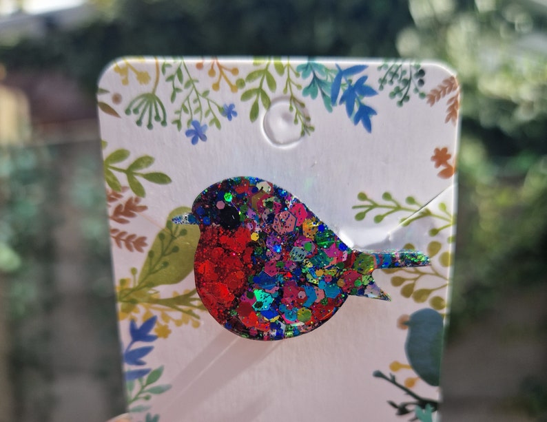 Peut inclure: Une broche en forme de rouge-gorge en paillettes rouges, bleues et vertes. Le rouge-gorge est un symbole populaire du printemps et des nouveaux d&eacute;parts.