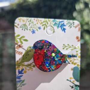 Peut inclure: Une broche en forme de rouge-gorge avec des paillettes rouges, bleues et vertes. Le rouge-gorge est en r&eacute;sine et a une finition brillante et scintillante.