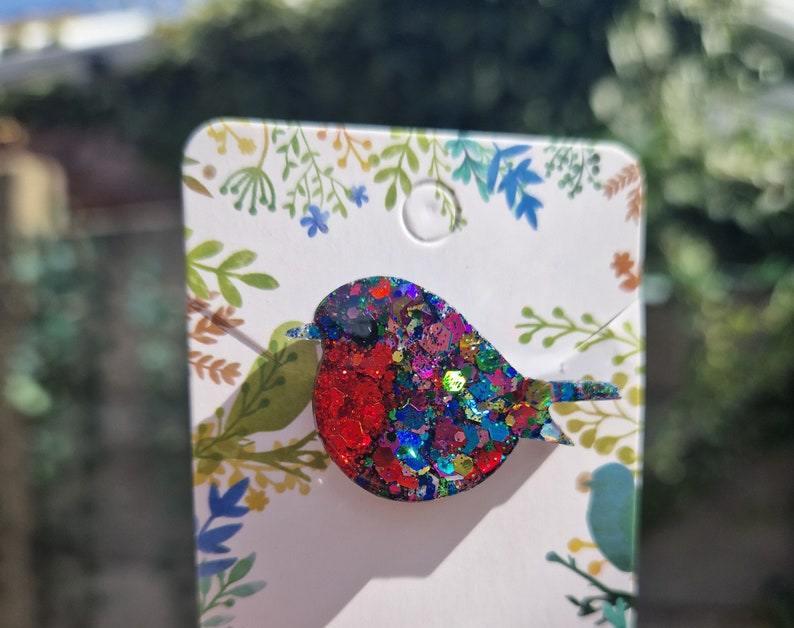 Peut inclure: Une broche en forme de rouge-gorge avec des paillettes rouges, bleues et vertes. Le rouge-gorge est en r&eacute;sine et a une finition brillante et scintillante.