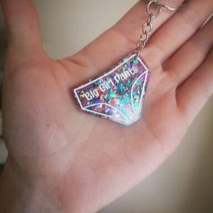 May include: A sparkly pink and blue keychain with a white outline of underwear and the text "Big Girl Pants".