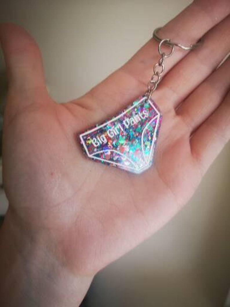 May include: A sparkly pink and blue keychain with a white outline of underwear and the text "Big Girl Pants".