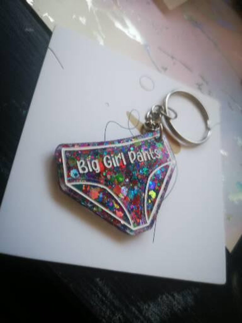 May include: A colourful glitter keychain shaped like underwear with the text "Big Girl Pants" in white lettering.