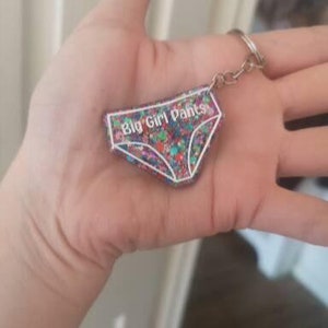 May include: A colourful glitter keychain shaped like underwear with the text "Big Girl Pants" in white.