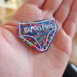 May include: A colourful glitter-filled resin keychain shaped like underwear with the text "Big Girl Pants" in white.