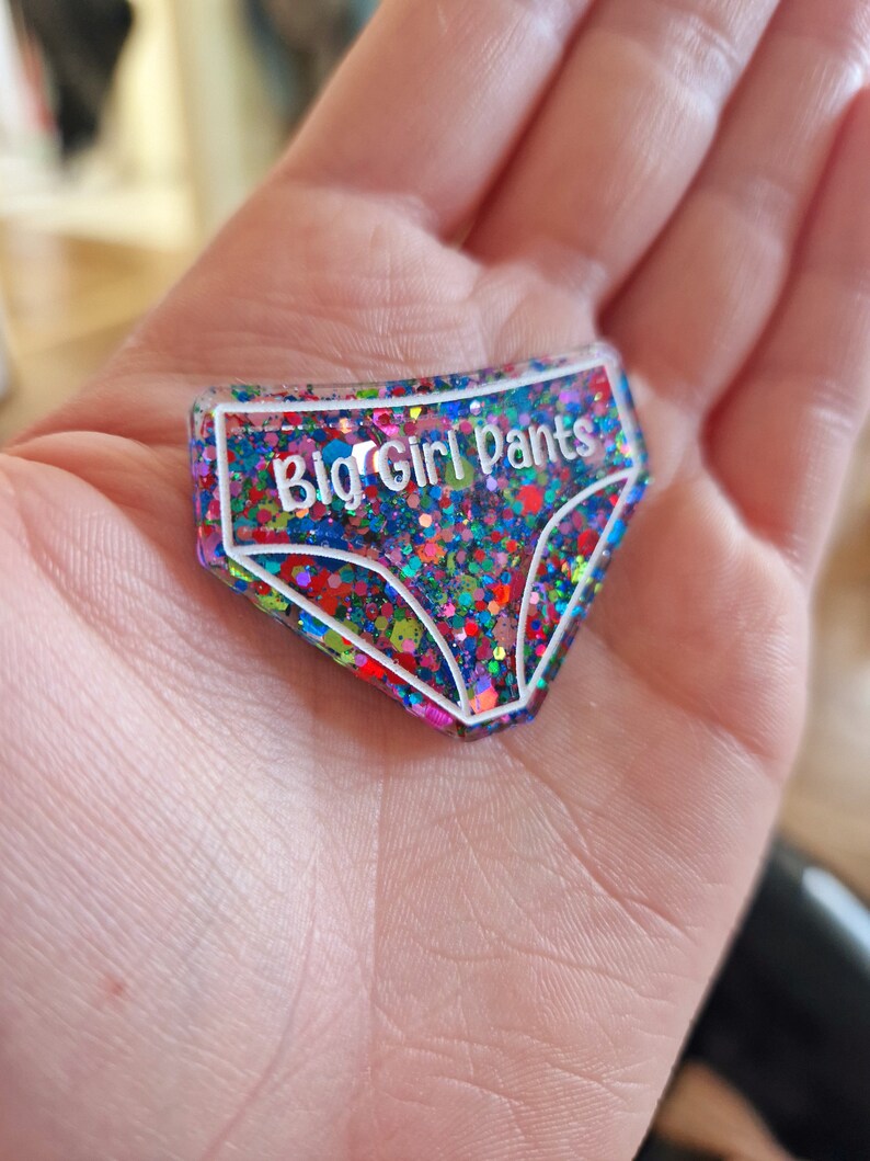 May include: A colourful glitter-filled resin keychain shaped like underwear with the text "Big Girl Pants" in white.