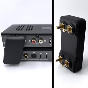 Puede incluir: Amplificador de audio negro con un conector negro y dorado. El amplificador tiene un panel frontal negro con una perilla plateada y un panel trasero negro con una variedad de puertos. El conector tiene dos pines dorados.