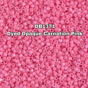 Könnte beinhalten: Ein Nahaufnahmebild einer großen Menge kleiner, undurchsichtiger, rosa Perlen. Die Perlen sind rund und haben ein Loch in der Mitte. Der Text "DB1371 Dyed Opaque Carnation Pink" ist im Bild sichtbar.