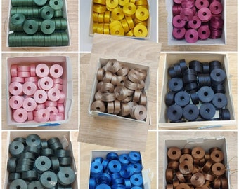 May include: Assortment of spools of thread in various colors, including black, blue, brown, green, pink, and yellow. The spools are arranged in rows in small boxes.