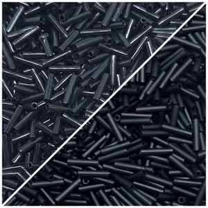 Może przedstawiać: Zbliżenie na czarne szklane koraliki. Koraliki są długie i cylindryczne, ułożone w przypadkowy wzór. Koraliki są błyszczące i odbijające światło.