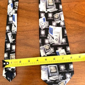 May include: Black necktie with a repeating pattern of computers, keyboards, and the words "e-mail" and "Inter-net." The tie is measured with a tape measure, showing a width of approximately 2 inches.