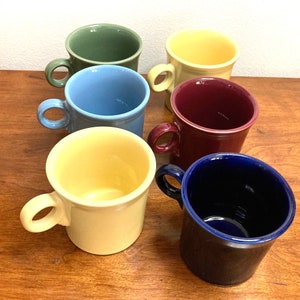 May include: Six ceramic mugs in different colors: green, yellow, blue, maroon, yellow, and blue. The mugs have a simple design with a single handle.