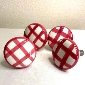 May include: Four round cabinet knobs with a red and white plaid pattern. The knobs are made of ceramic and have a glossy finish. Each knob has a metal screw for easy installation.