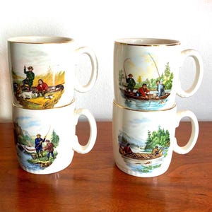 May include: Four white ceramic mugs with gold rims, each featuring a different outdoor fishing scene. The illustrations depict men fishing from boats and the riverbank. The mugs have a classic, vintage aesthetic.