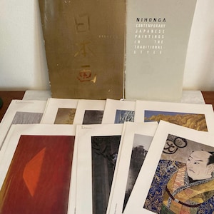 May include: A collection of art prints and two books titled Nihonga Contemporary Japanese Paintings in the Traditional Style. The books have gold and light gray covers. The prints feature various artistic scenes including a portrait of a person in patterned clothing, landscapes, and abstract red shapes.