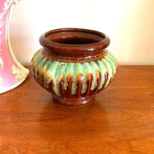 May include: A brown and green ceramic planter with a textured, ribbed design. The planter has a wide, round base and a slightly narrower opening.