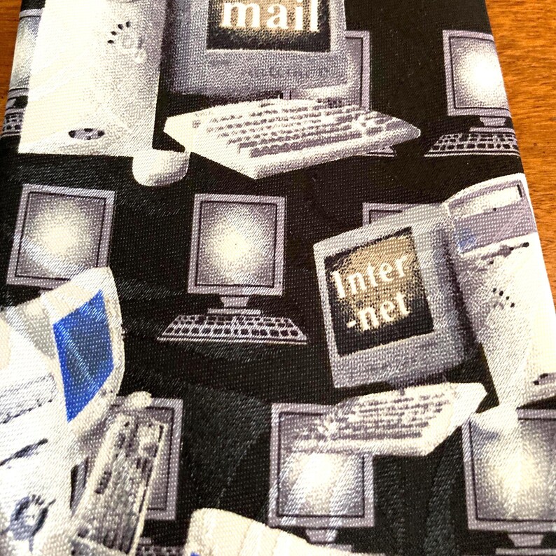May include: A black necktie with a repeating pattern of computer monitors, keyboards, and computer towers in shades of gray and white. The word "mail" is visible on one monitor, and "Internet" is on another.