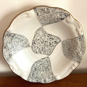 May include: A white ceramic bowl with a black and white geometric pattern. The bowl has a scalloped edge and a gold rim.
