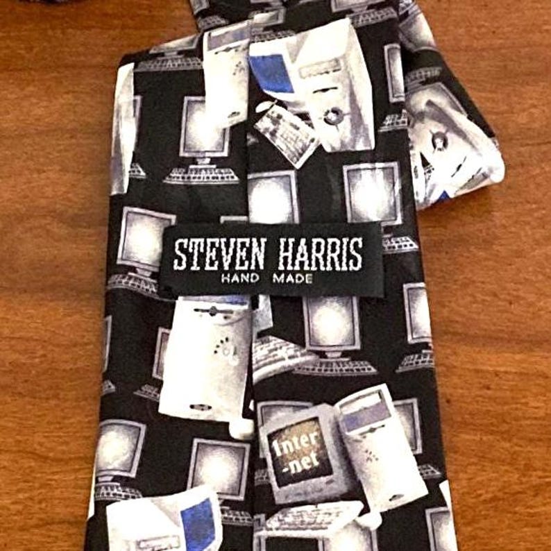 May include: A black necktie with a repeating pattern of white computer monitors and the word "Internet" on some. The label reads "Steven Harris Hand Made".