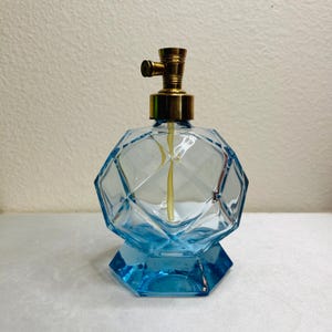 May include: A vintage blue glass perfume bottle with a geometric design. The bottle has a brass atomizer and a faceted, diamond-like pattern. The base is a darker shade of blue, and the bottle is empty.