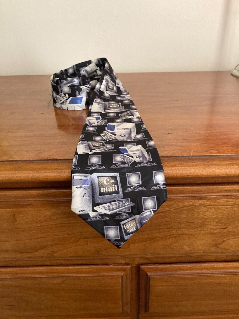 May include: A black necktie featuring a repeating pattern of vintage computer monitors, keyboards, and computer towers in shades of white and gray. The tie also has the words "e-mail" and "internet" printed on it.