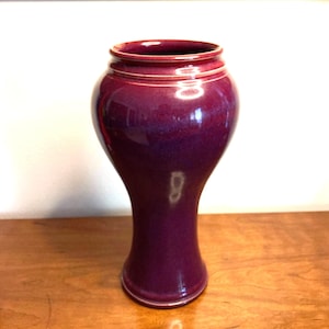 May include: A tall, slender vase with a deep purple glaze. The vase has a rounded base and a narrow neck.