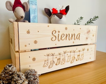 May include: A wooden crate with the name "Sienna" engraved on the front. The crate is decorated with snowflakes and a string of Christmas stockings.