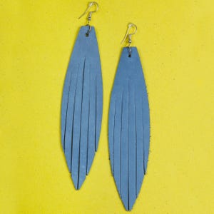 Può includere: Un paio di lunghi orecchini in pelle blu con dettagli a frangia. Gli orecchini sono appesi a ganci argentati.