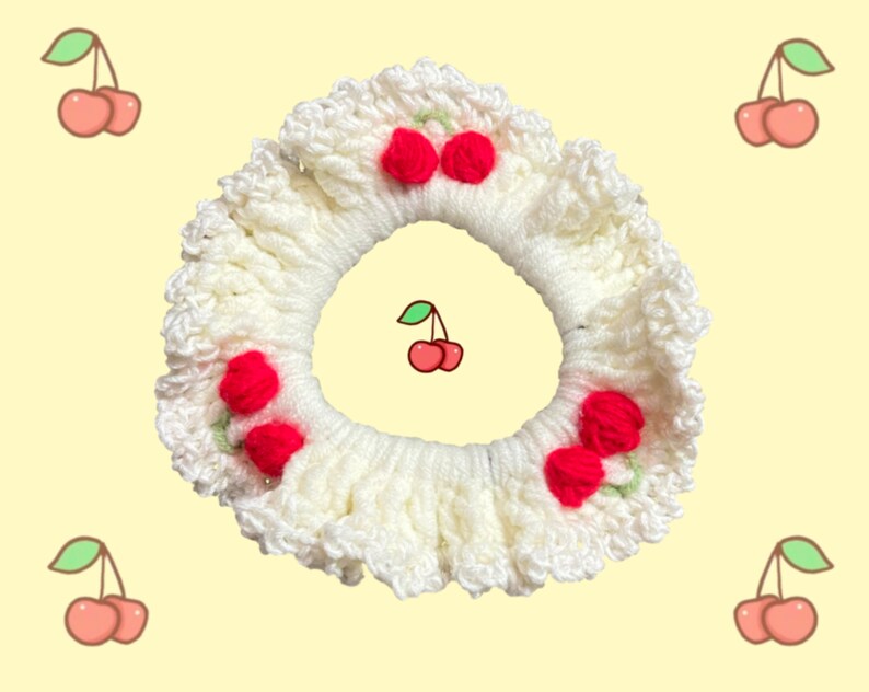 May include: White crocheted hair scrunchie with red cherry embellishments. The scrunchie has a ruffled edge and is decorated with five cherries.